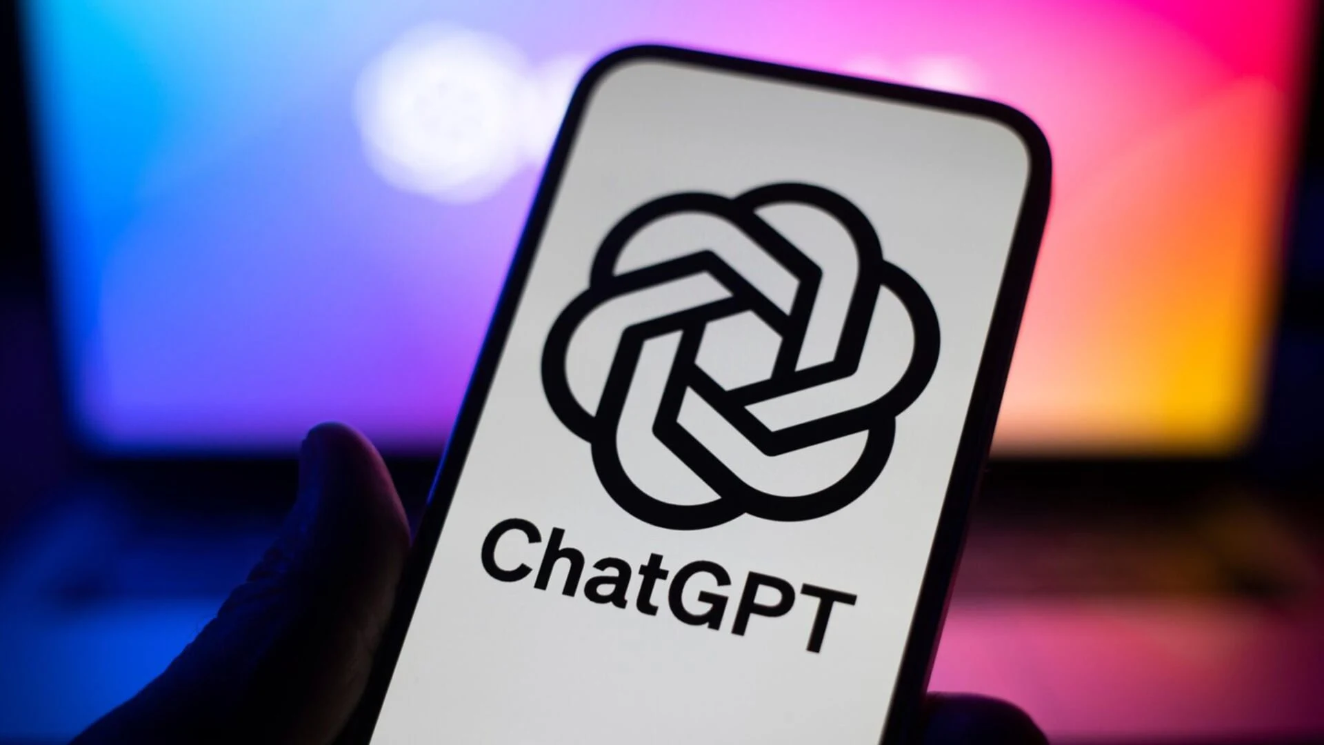 A hand holding a phone that displays the ChatGPT logo against a colorful screen glow.